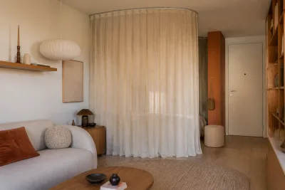 Coin salon d'un petit appartement avec rideau pleine hauteur formant une courbe, tapis ovale et table aux bords adoucis